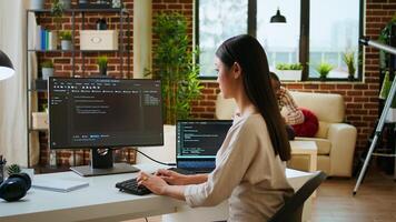 Asian programmer seen typing code for a user interface design on dual monitors, working in a digital workspace. Woman coder working on software engineering and front end development. Camera A. photo