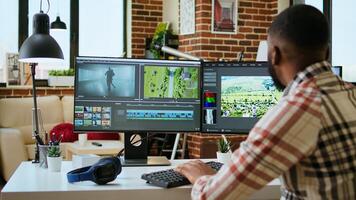 African american man editor working in production industry, does color grading and editing a film project on dual monitors. Showing the creative process with tech tools. Camera A. photo