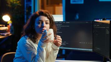 Portrait of smiling IT specialist drinking coffee while looking for company security vulnerabilities and preventing malware infections. Programmer enjoying hot beverage while writing code, camera A photo