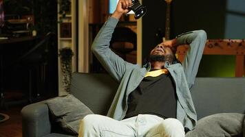 Enthusiastic gamer on couch using controller and headphones to play videogame in neon lit apartment. Player in RGB illuminated living room using high tech gaming console joystick, camera A photo