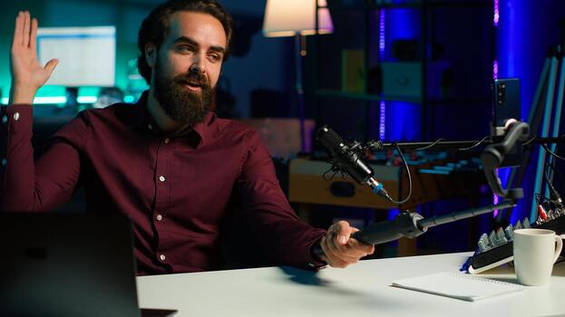 Content creator talking in front on cellphone attached to selfie stick in studio, chatting with viewers using recording mic. Man using phone camera and professional microphone to record vlog, camera A photo