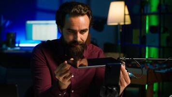 Tech specialist presenting tablet in entry level low budget price range to interested viewers, filming with smartphone on tripod. Man reviewing digital device, recording with mobile phone, camera A photo