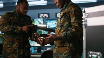 Operatives conducing special operation, doing checkup on rifles and pistols, preparing to attack enemy. African american military units in command post packing guns for assault mission, camera A photo