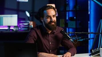 Content creator talking about himself while recording with production gear in home studio interior illuminated with RGB lights at night. Entertainer talking in professional microphone, camera A photo