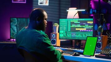 Young musician mixing and mastering songs next to isolated mockup display, operating on digital audio software to add sound effects on new tracks recorded. Audio engineer in home studio. Camera A. photo