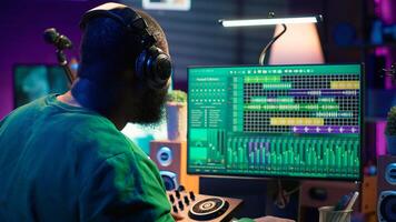 Young musician twisting knobs and mixing tunes with a console, following record settings on a digital software interface. Artist composer producing new music hits in his home studio. Camera A. photo