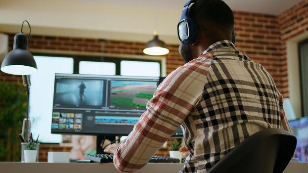 African american filmmaker editing a shoot in post production, using a modern tech setup for creative project. Living room workspace with editing software and dual monitors. Camera A. photo