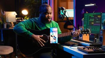 Professional composer teaching guitar lessons online on master class, recording himself playing acoustic instrument accords and explaining notes for tutorial. Young musician making vlogs. Camera A. photo
