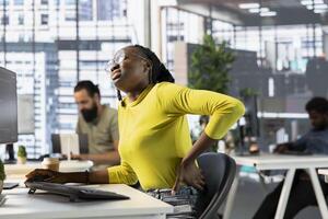 Developer suffering backpain from bad posture on office chair while fixing applications issues. Fatigued IT expert feeling muscle strain while optimizing company software for improved performance photo