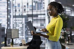 Cybersecurity expert using laptop to look for company security vulnerabilities, comparing with computer monitors. Programmer installing fortified code on laptop, crosschecking with PC screens photo