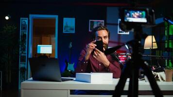 Tech guru using professional camera to film technology review of new cellphone, doing unboxing . Content creator showing phone box to subscribers, recording with high tech gear, camera B photo