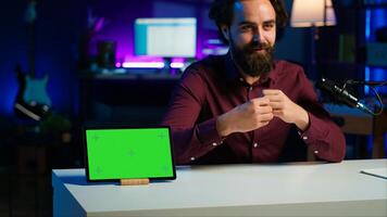 Tech specialist presenting mockup tablet to interested viewers, filming with professional mic. Man reviewing green screen digital device, recording with specialized equipment, camera A photo