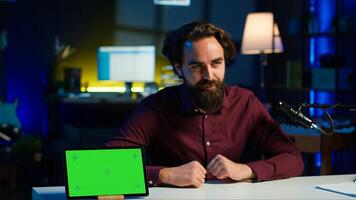 Tech engineer presenting green screen tablet in low budget price range, filming from dimly lit home studio. Content creator reviewing mockup digital device in front of online audience, camera A photo