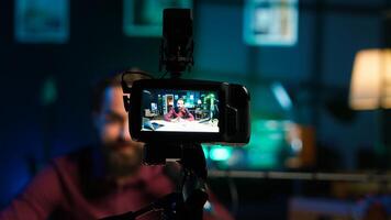 Content creator hosting online show in rgb lights studio, shooting vlog using professional gear. Vlogger presenting informations during streaming service broadcast filmed with camera, camera A photo