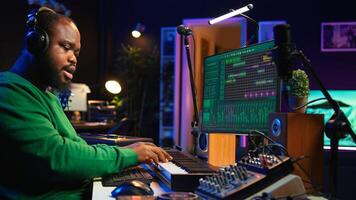 Sound producer working with console and electronic keyboard to create perfect tracks for his songs, recording and editing audio. Music composer adjusts volume levels on pre amp knobs. Camera B. photo