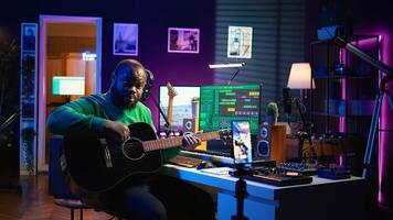 Professional composer teaching guitar lessons online on master class, recording himself playing acoustic instrument accords and explaining notes for tutorial. Young musician making vlogs. Camera B. photo