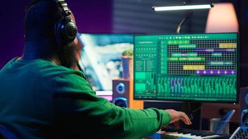 Audio engineer working in home studio with digital software on pc, playing piano keys and editing audio recordings. Musician producer creating tracks on midi controller keyboard notes. Camera A. photo