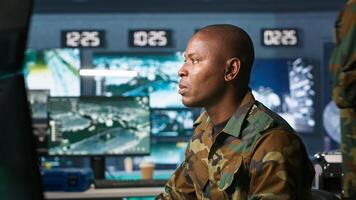 Intelligence operative in military base doing surveillance with digital radar equipment, operating missile systems. African american man monitoring army HQ CCTV for any unauthorized activity, camera A photo