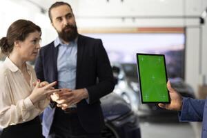 Car dealership salesperson reading text on green screen tablet, providing information about available models. Showroom agent holding chroma key device, negotiating vehicle prices with client photo
