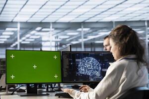 Woman in AI data center coding on green screen computers, upgrading equipment. IT engineers at PC desk overseeing artificial intelligence server clusters using mockup monitor photo