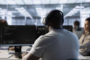 System administrator working in computer network security data center, enjoying music. Employee wearing headphones monitoring server racks energy consumption, listening music photo
