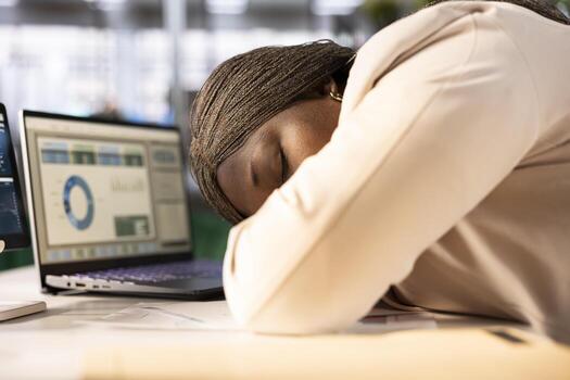 Exhausted businesswoman falling asleep at desk while monitoring and analyzing sales performance metrics and trends on laptop. Tired CEO dozing off while managing budgets on notebook photo