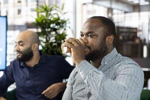 Man in startup company enjoying cup of coffee, looking at financial business documents. Worker in office drinking caffeinated beverage to gain energy, trying to finish tedious paperwork photo