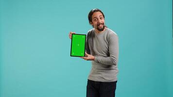 Happy man holding green screen tablet, doing recommendation. Cheerful person presenting mockup device, showing positive feedback, isolated over studio background, camera A photo