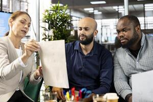 Multiracial team of accountants looking over revenue figures on documents in office. Multiethnic workers in office comparing company statistical numbers, working hard to finish job before deadline photo
