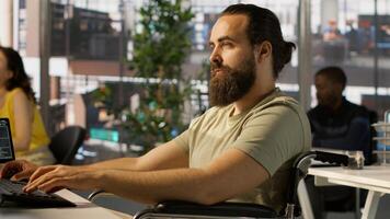 System administrator with disability in inclusive workspace training machine learning models. IT specialist with paraplegia monitoring and maintaining company systems, camera A photo