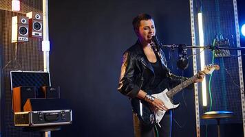 Rock star woman in a leather jacket playing an electric guitar in studio, rocking out to powerful music in a live performance. Fierce artist entertainer creating wild rebellious atmosphere. Camera A. photo