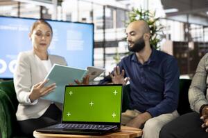 Chroma key laptop next to team of office clerks looking over revenue figures in office. Staff members comparing company statistical numbers on isolated screen notebook in workspace photo