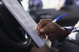Person in car dealership writing signature on contract with salesperson after having concerns addressed during test drive. Close up of client completing deal documents to pay for vehicle photo
