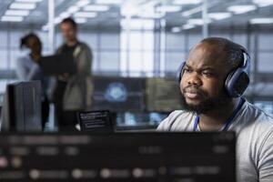 Admin in server hub listening music and ensuring compliance with industry standards and regulatory requirements. Data center worker wearing headphones enjoying songs and conducting security audits photo