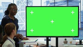 Diverse work team discusses corporate strategies with a big green screen, meeting in high end boardroom to examine market trends. Sharing new ideas for business growth and expansion. Camera A. photo