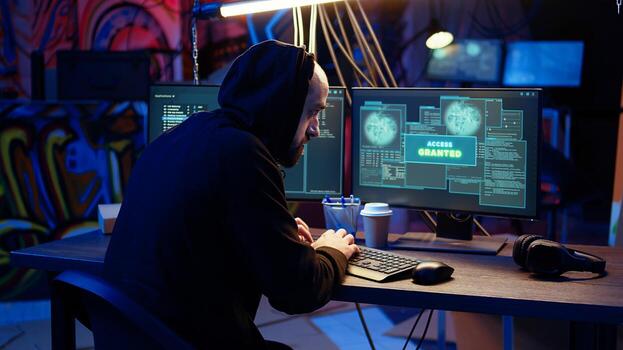 Jolly hacker in graffiti painted hideout excited after managing to steal valuable data, using phishing technique that tricks users into revealing passwords, getting access granted, zoom in shot photo