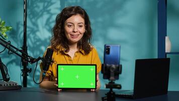 Upbeat technology specialist at home holding newly launched green screen tablet in hand, presenting specs. Joyous internet star doing mockup portable digital device review for viewers, camera A photo