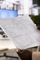 Architect looking at blueprint to scale of house room drawn in architectural engineering software. Close up of designer in office handling the planning and designing of building photo