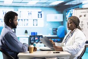 General practitioner reviewing x ray imaging at checkup with male patient, offering her professional expertise to ensure wellness. Medic doing scan interpretation with a man in the office. photo