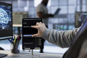 Technician optimizing data center workspace with tablet for maximum efficiency and uptime. Programmer in server hub maintaining optimal network performance, performing backups using device, close up photo