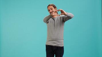 Portrait of joyful friendly man doing heart symbol shape gesture with hands. Smiling nurturing person showing love gesturing, isolated over blue studio background, camera A photo
