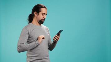 Portrait of smiling man scrolling on smartphone touchscreen, using mobile phone to check social media feed. Cheerful person browsing online websites, isolated over studio background, camera B photo