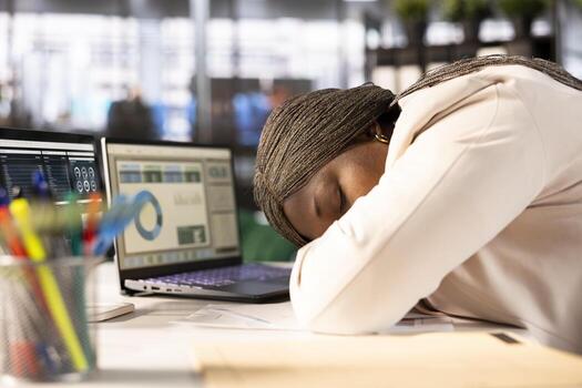 Overworked woman falling asleep at desk while looking over statistics charts on laptop, researching data. Tired worker napping in office on notebook while doing research for marketing project photo