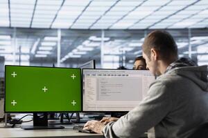 Engineer in server farm using green screen PC to repair equipment storing datasets. IT professional using mockup computer to do debugging on rigs doing computational operations photo