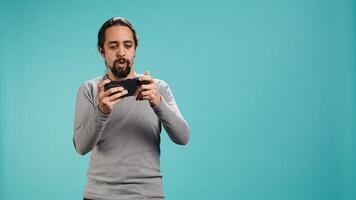 Man playing intense singleplayer videogames on smartphone, enjoying hobby. Gamer enjoying entertaining interactive game on phone, having fun, isolated over studio background, camera B photo
