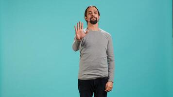 Assertive man doing stop hand gesture sign, studio backdrop. Annoyed person doing firm halt sign gesturing, wishing to end concept, isolated over blue studio background, camera A photo