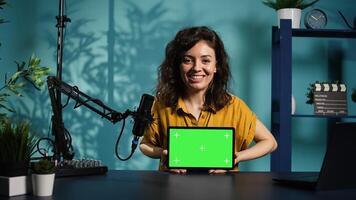 Cheerful media star being sponsored by partnering brand to do mockup tablet unboxing content. Upbeat tech expert does influencer marketing, presenting green screen device, camera B photo