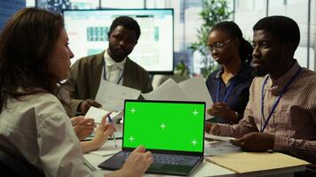 Diverse team of business associates looking at mockup chroma key screen during executive board meeting, utilizing smart technology. Enterprise staff develop effective business strategies. Camera B. photo