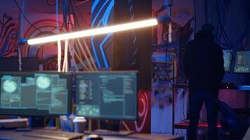 Hooded hacker arrives in neon lit underground shelter filled with graffiti artwork. Cybercriminal enters colorful painted basement, starting work on script that can crash businesses servers, camera B photo
