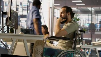 IT worker with disability sitting in wheelchair in office working at computer desk, focused on testing programs. Software engineer with paraplegia in inclusive workplace checking code on PC, camera A photo